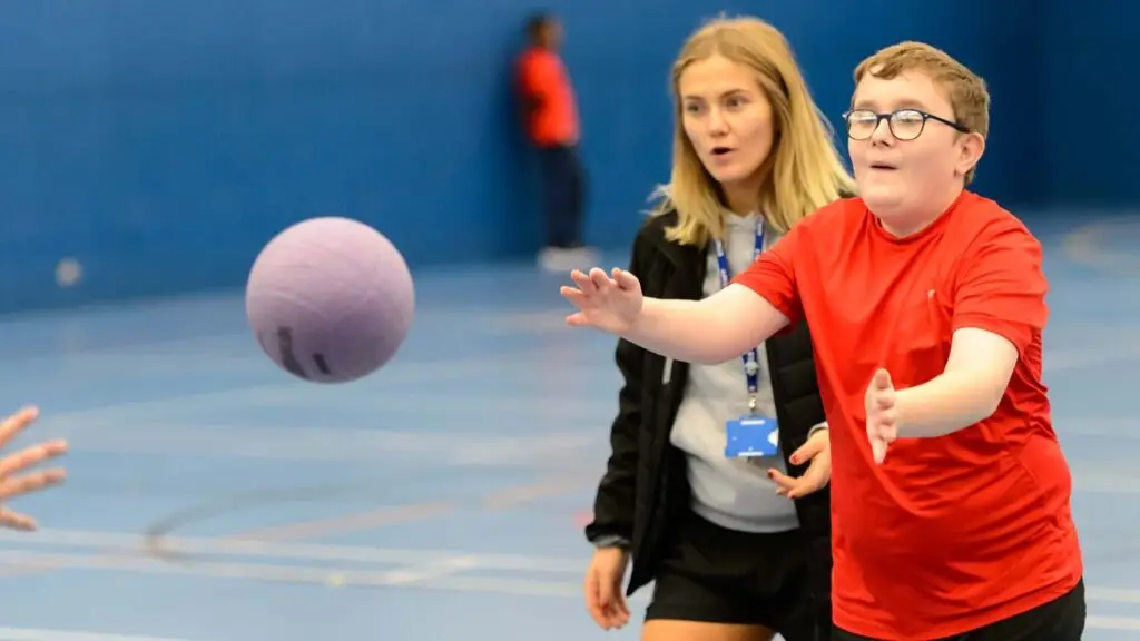 A child throwing a ball while being supported by a coach