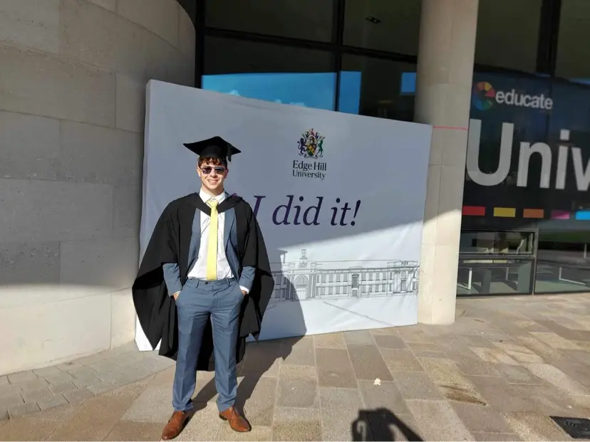 Jake Jose in his graduation cap and gown in front of a sign saying 'I did it!'