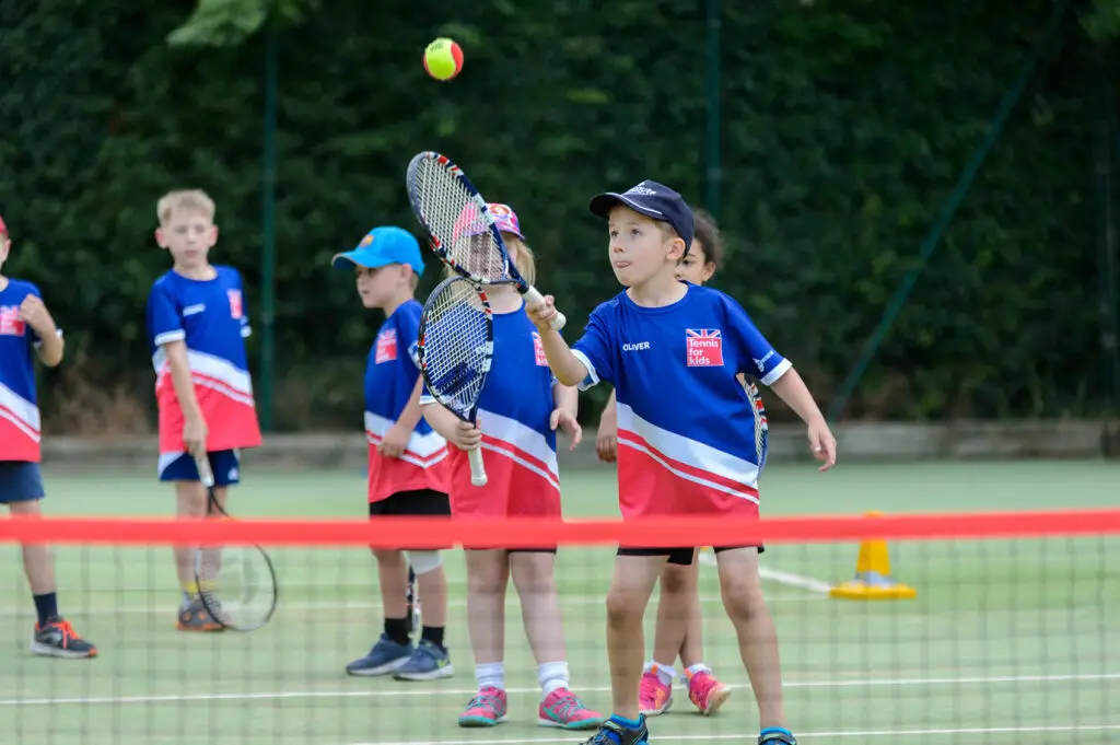 A group of children playing tennis wearing 'Tennis for kids' t-shirts