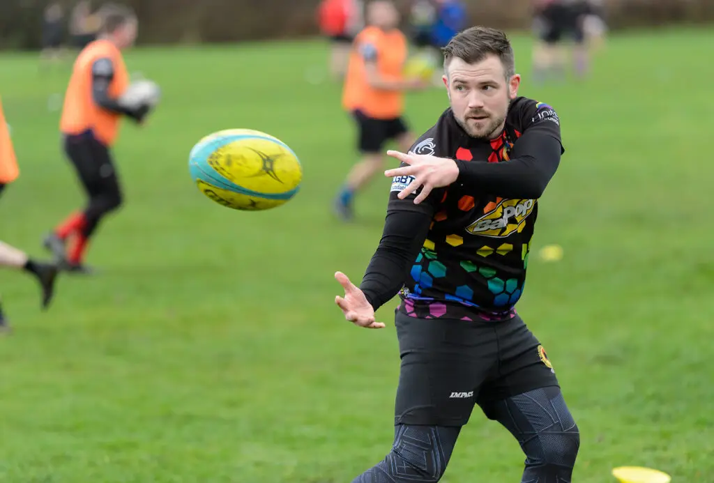 An LGBT rugby player in a pride jersey catches a rugby ball