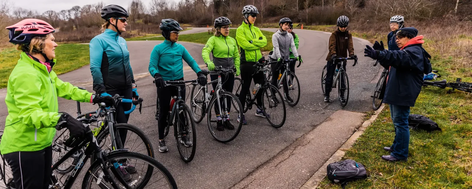 A group of cyclists at the side of a road listening to a coach