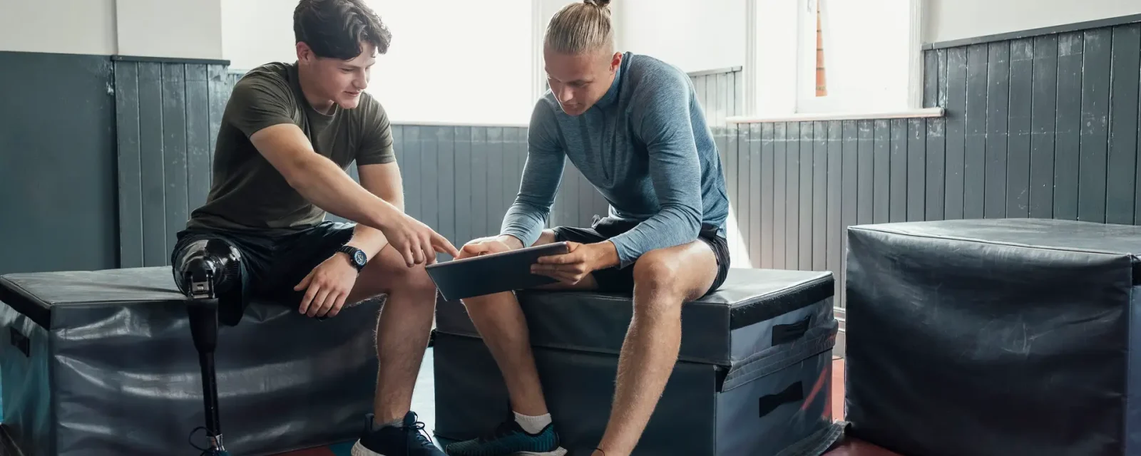 Young male with prosthetic leg sat talking to personal trainer with digital tablet.