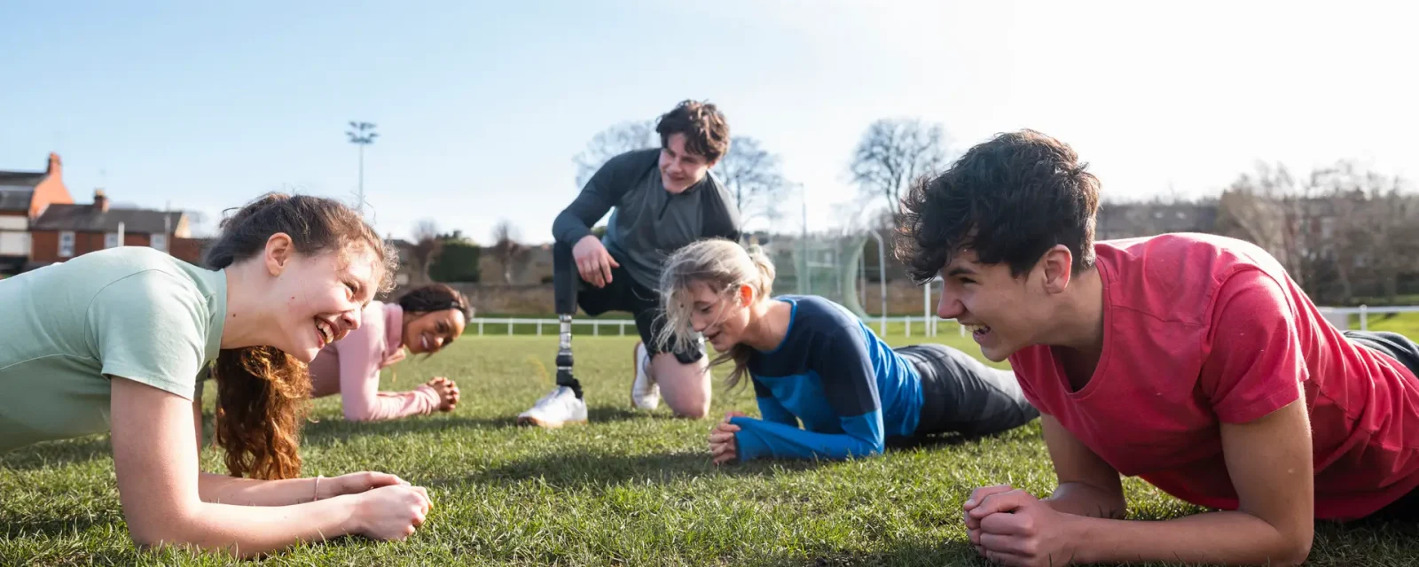 A group of teenagers holding a plank in the press up position on an outdoor sportig field.