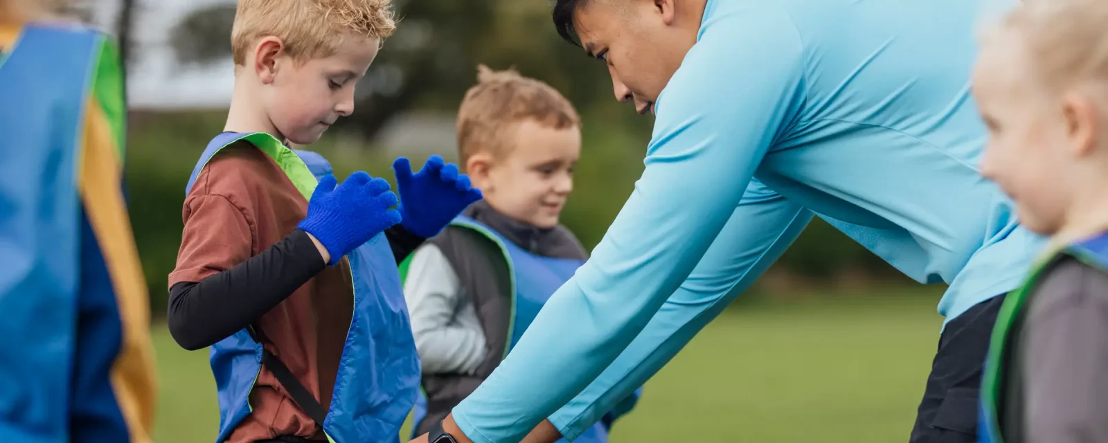 A football coach helps a boy put on a sports bib