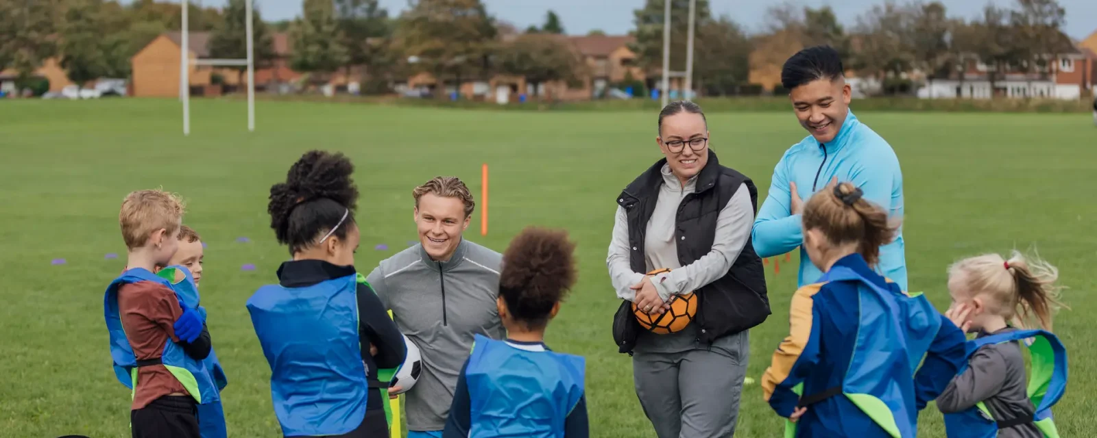 Coaches teaching a group of under 10's football on a pitch.