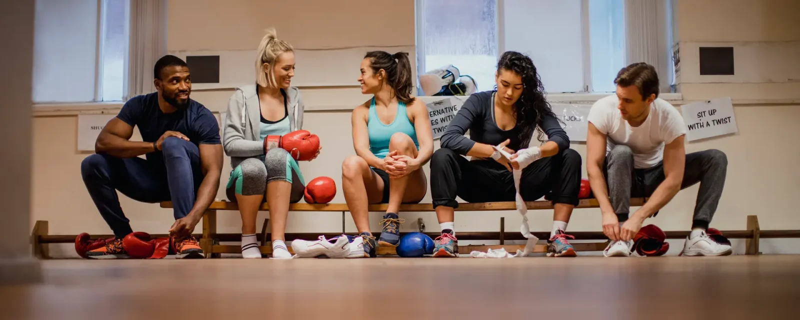 A group preparing for an exercise class in a gym wrapping their hands with bandages before boxing training.