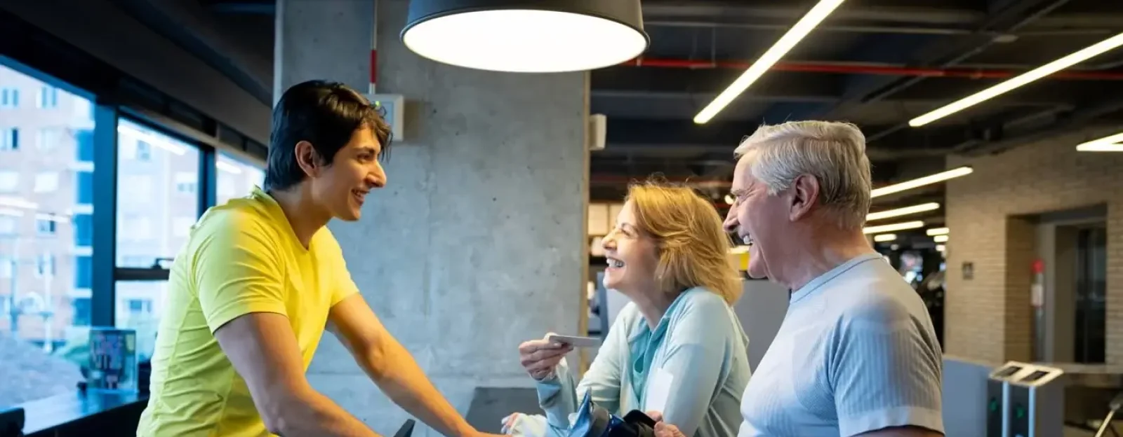 A recreation assistant speaking to two clients at a gym's reception desk